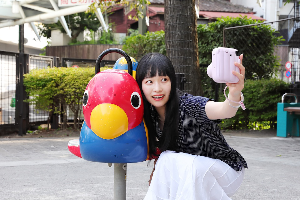 公園の遊具が写るようにセルフィーを撮影している様子