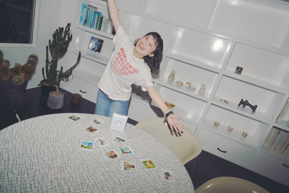 SQUARE Link本体や撮影したチェキプリントが並べられたテーブルと両手を広げているなちさんの写真