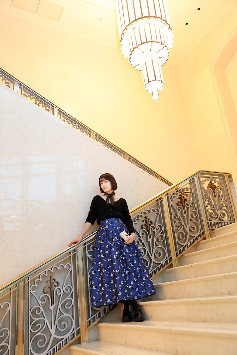 階段の中ほどで手すりに寄りかかって立っている甲斐さん