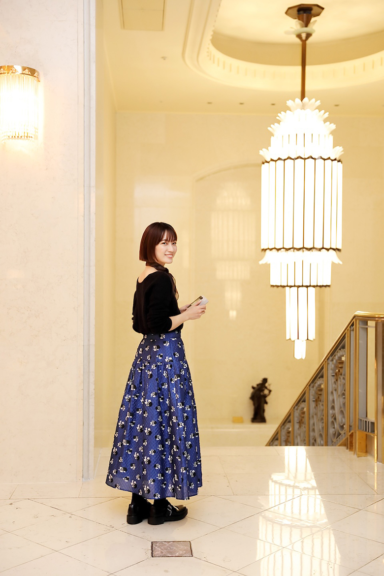 階段にある大きなシャンデリアと近くに立っている甲斐さん