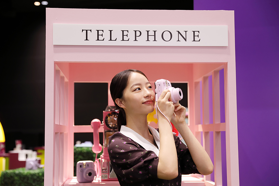 電話ボックスのセットの前でmini 13のファインダーをのぞいている池端さん