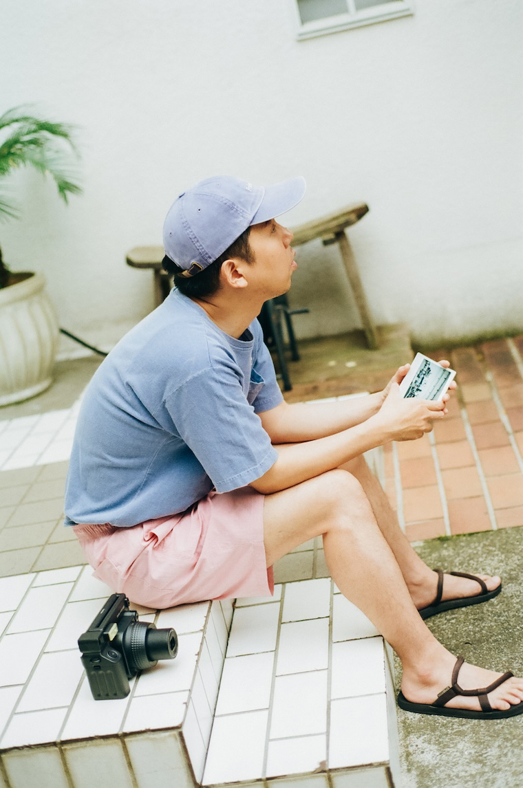屋外の階段に座ってチェキプリントを手に持っている安部さん