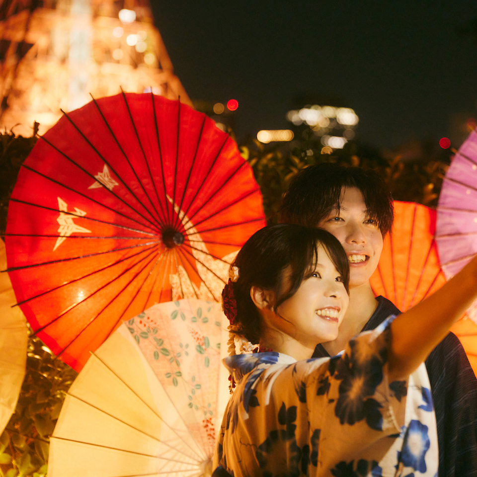 東京タワーを背景に、浴衣を着た男女がセルフィーを撮影している写真