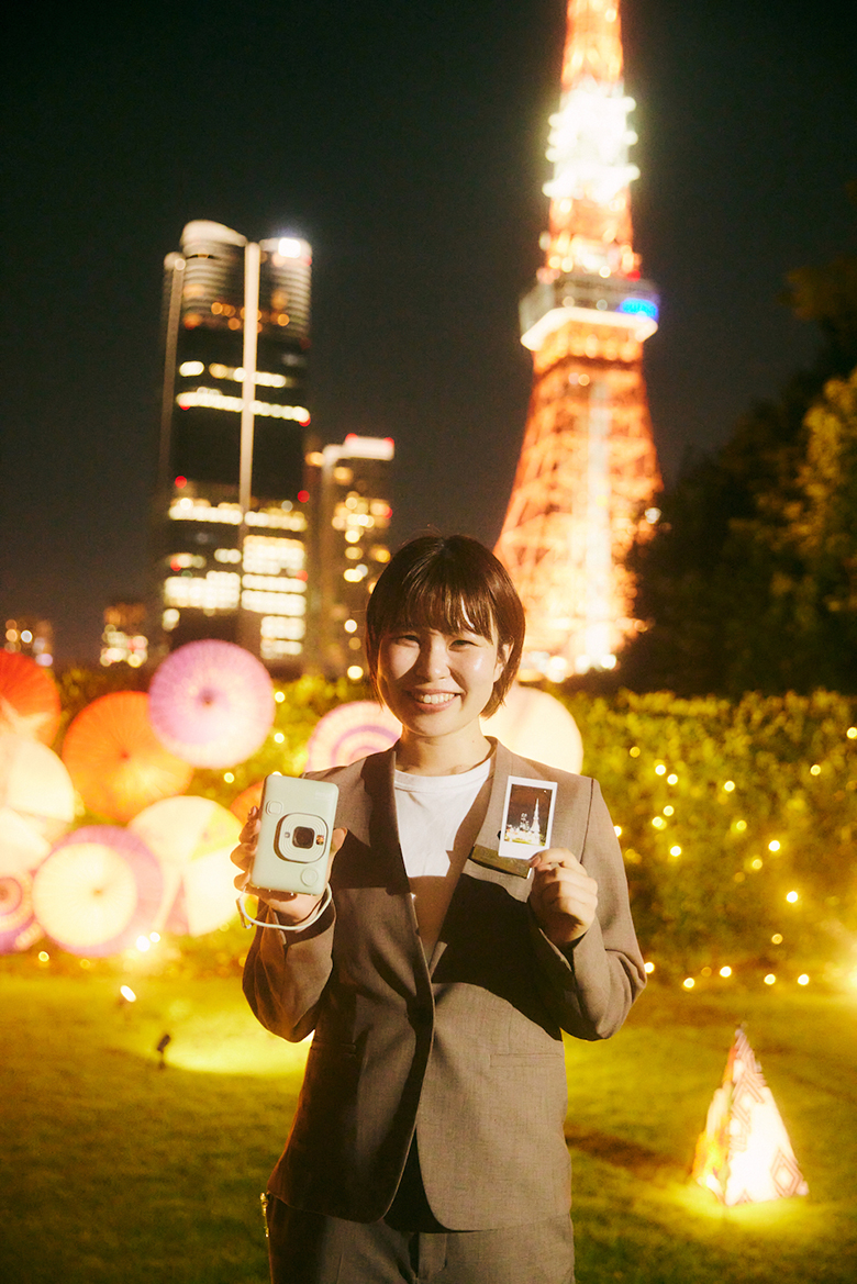東京タワーを背景にして、mini LiPlayとチェキプリントを手に持っている山口さんの写真