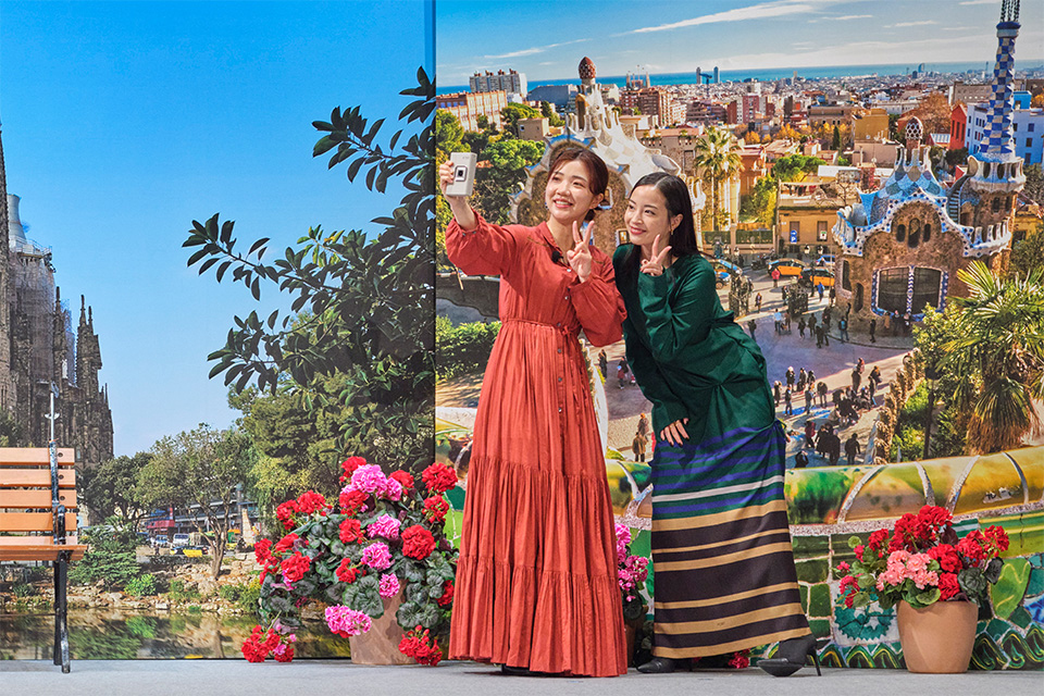 スペインの街並みがプリントされたセットを背景にセルフィーを撮影している写真