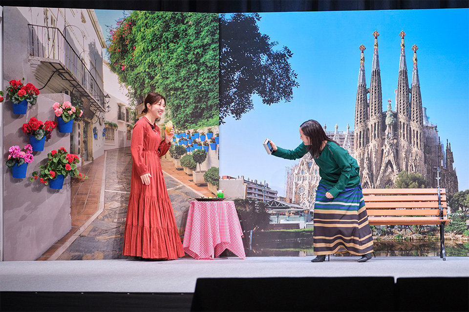 スペインの街並みがプリントされたセットを背景に広瀬さんが福田さんを撮影している写真
